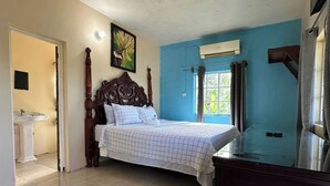 Un dormitorio con una cama grande, cabecera de madera, ventana con cortinas, aire acondicionado de pared y suelo de baldosas.