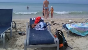 Una playa con sillas de descanso, una pelota de playa y una tabla de surf.