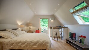 Een slaapkamer met een groot bed, een televisie, een bureau en een raam met uitzicht op groen.