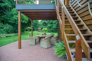 A covered patio with wicker furniture, a brick floor, and a wooden staircase.