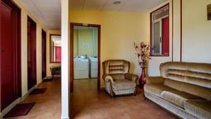 A hallway with a sofa, a chair, and a vase with flowers. - Albergue Vía Láctea - Hostel (Arzua)
