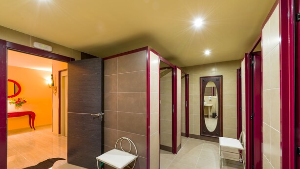 A modern bathroom with a mirror, a bench, and a door leading to another room. - Albergue Vía Láctea - Hostel (Arzua)