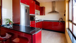 A modern kitchen with red cabinetry, stainless steel appliances, and a black countertop. - Albergue Vía Láctea - Hostel (Arzua)
