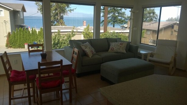 A living room with a view of the sea, a sofa, a dining table, and a chair.