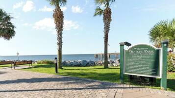 A sign for Neptune Park with a view of the ocean and a pier in the background.