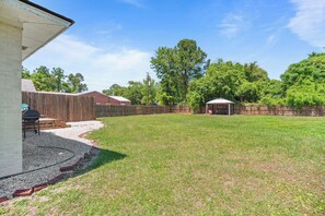 A backyard with a patio, a barbecue area, and a fenced enclosure. - Beach House -optional BIKES - Walk 2 Shops & Fun (Saint Simons Island)
