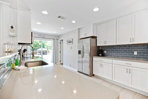 A modern kitchen with white cabinets, a stainless steel refrigerator, and a tiled backsplash. - Beach House -optional BIKES - Walk 2 Shops & Fun (Saint Simons Island)