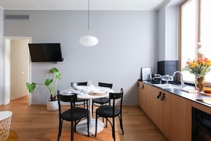 A modern kitchen with a dining area, wooden cabinets, a flat-screen TV, and a potted plant. - Vitruvio (Milan)