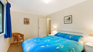 Una camera da letto con un letto, una sedia, un comodino, una lampada e una porta.