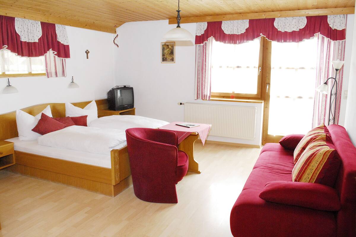 Ein Zimmer mit einem hölzernen Bett, einem roten Sofa, einem Holztisch und einem Fernseher.