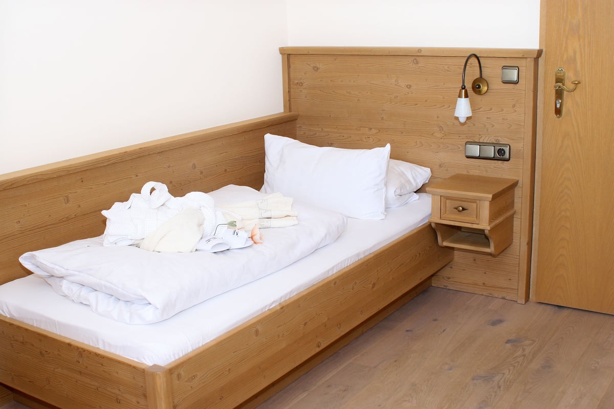 Ein hölzernes Bett mit weißer Bettwäsche, ein Nachttisch und ein Beistelltisch mit einer Lampe.