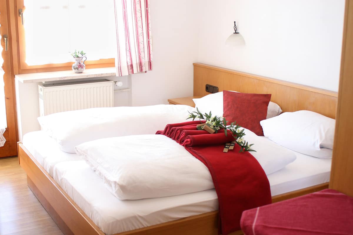 Ein Doppelbett mit weißer Bettwäsche, einer roten Tagesdecke und einem kleinen Blumentopf auf dem Nachttisch.