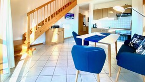 A modern kitchen with a wooden staircase, a dining area with blue chairs, and a kitchen island. - Haus Vierjahreszeiten (Bodenmais)