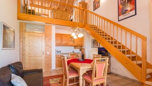 A cozy living room with a wooden staircase, a dining area with a red tablecloth, and a kitchen with wooden cabinets. - Haus Vierjahreszeiten (Bodenmais)