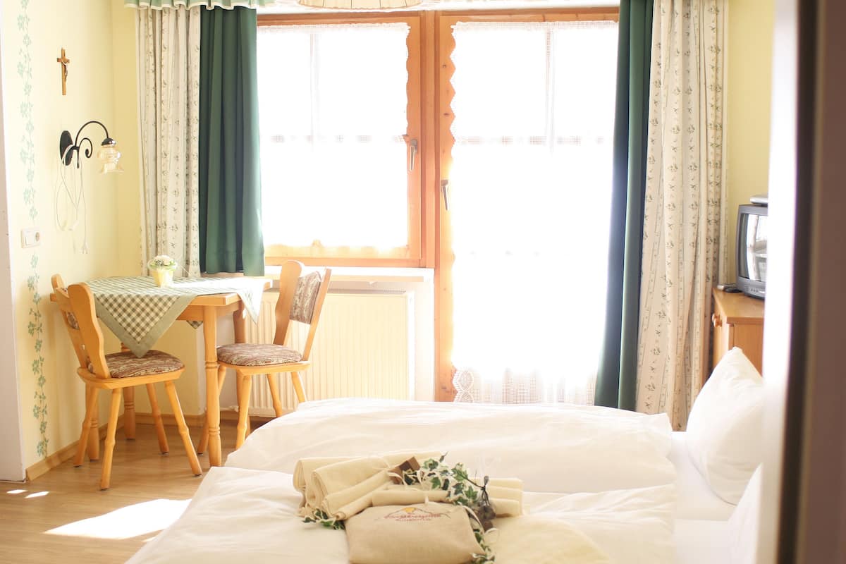 Ein Zimmer mit einem Bett, einem Tisch mit Stühlen, einem Fernseher und einem Fenster mit Vorhängen.