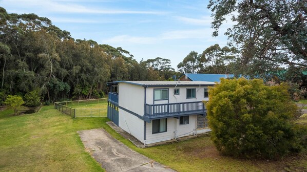 A two-story house with a balcony, surrounded by a grassy yard and dense trees. - Pet-friendly Beach House @ Kianga (KIANGA)