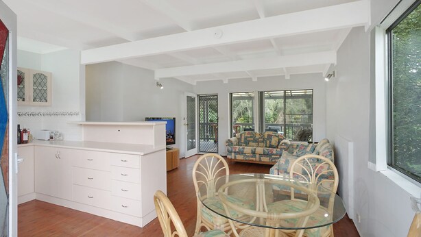 A spacious living area with a glass dining table surrounded by wicker chairs, a white cabinet, and a sofa with patterned cushions.