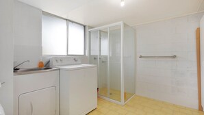 A compact kitchen with a washing machine, a sink, and a glass-enclosed shower.