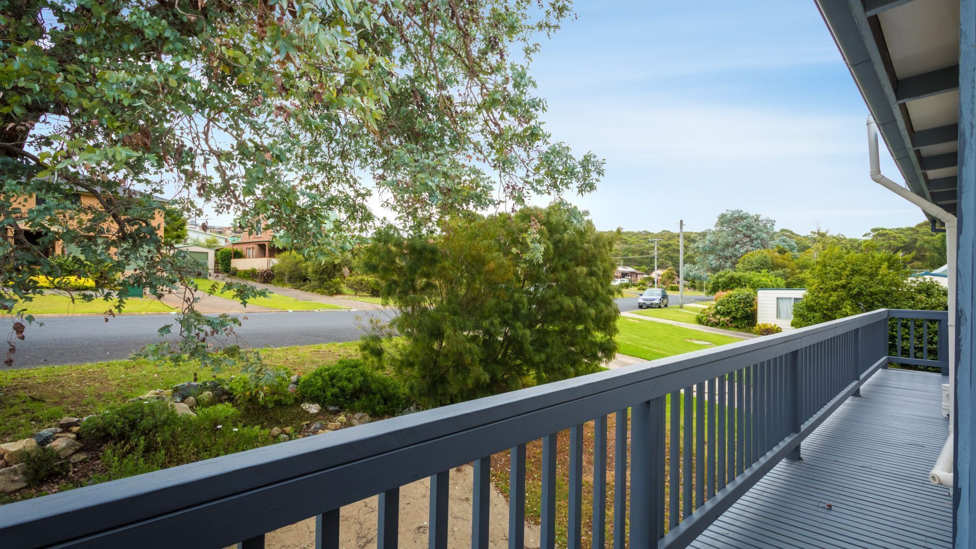 A residential property with a wooden deck, a view of a street, and a large tree in the foreground.