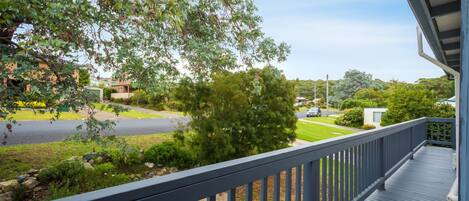 A residential property with a wooden deck, a view of a street, and a large tree in the foreground.