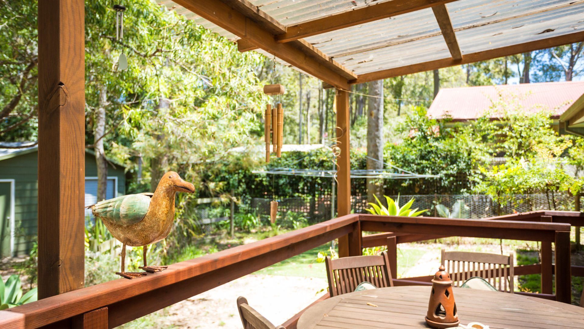 A wooden deck with a table and chairs, a bird sculpture, and a hanging wind chime.