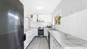 Eine moderne Küche mit weißen Schränken, einem Edelstahlkühlschrank, einem eingebauten Backofen und einer Marmorarbeitsplatte.