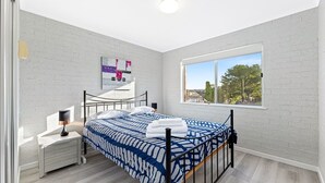 Ein modernes Schlafzimmer mit Bett, Nachttisch, Lampe und einem großen Fenster mit Blick.