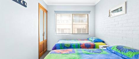 Una habitación pequeña y luminosa con dos camas, una ventana y una puerta.