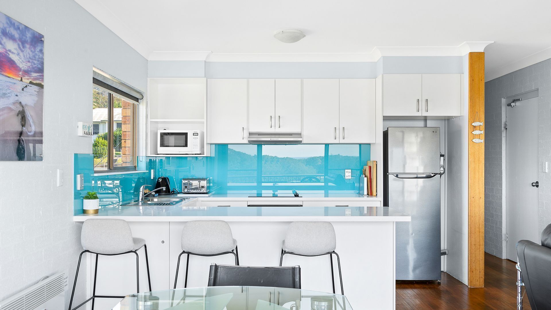 A modern kitchen with white cabinets, a stainless steel refrigerator, a microwave, and a glass island with bar stools.