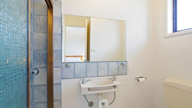 Un baño con pared de azulejos, un lavamanos, un espejo y un inodoro.