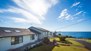 Une maison située sur la côte, avec un toit en tuiles, de grandes fenêtres et une vue sur la mer.