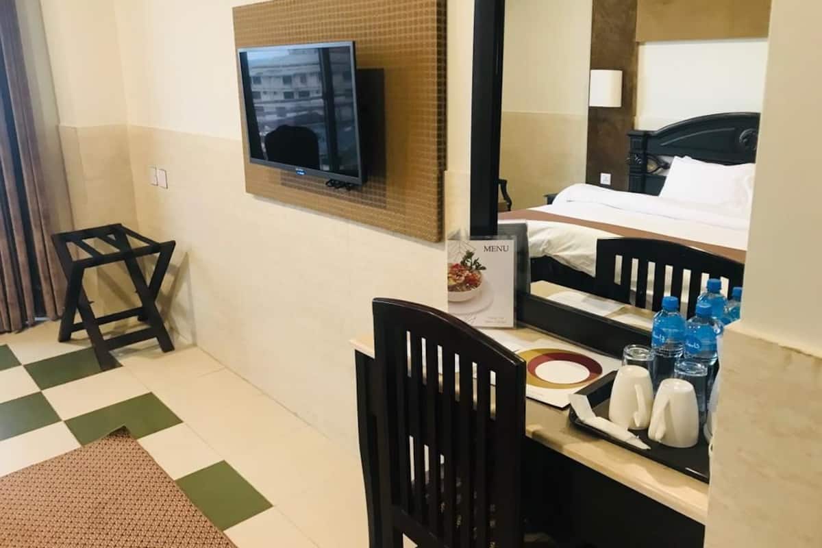 A hotel room with a bed, a television mounted on the wall, a desk with a chair, and a small table with a menu and water bottles.
