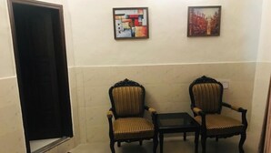 A room with two armchairs and a small table, a door, and two framed pictures on the wall. - Hotel One Mall Road Murree (Murree)