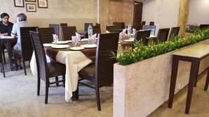 A dining area with tables set for multiple people, chairs, and a decorative planter with greenery. - Hotel One Mall Road Murree (Murree)
