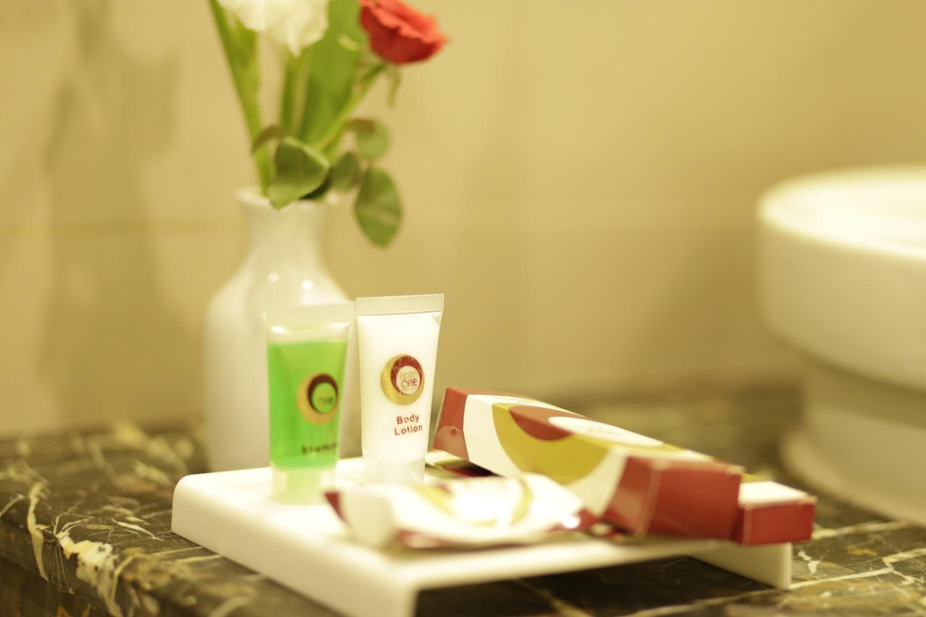 Un tocador de baño con artículos de aseo personal, incluyendo una botella verde, un tubo blanco con la etiqueta 'Loción Corporal' y una caja roja y blanca.