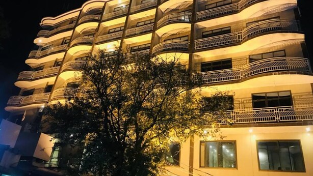 Un hotel de varios pisos con balcones en cada planta, un árbol en primer plano y un ambiente nocturno.