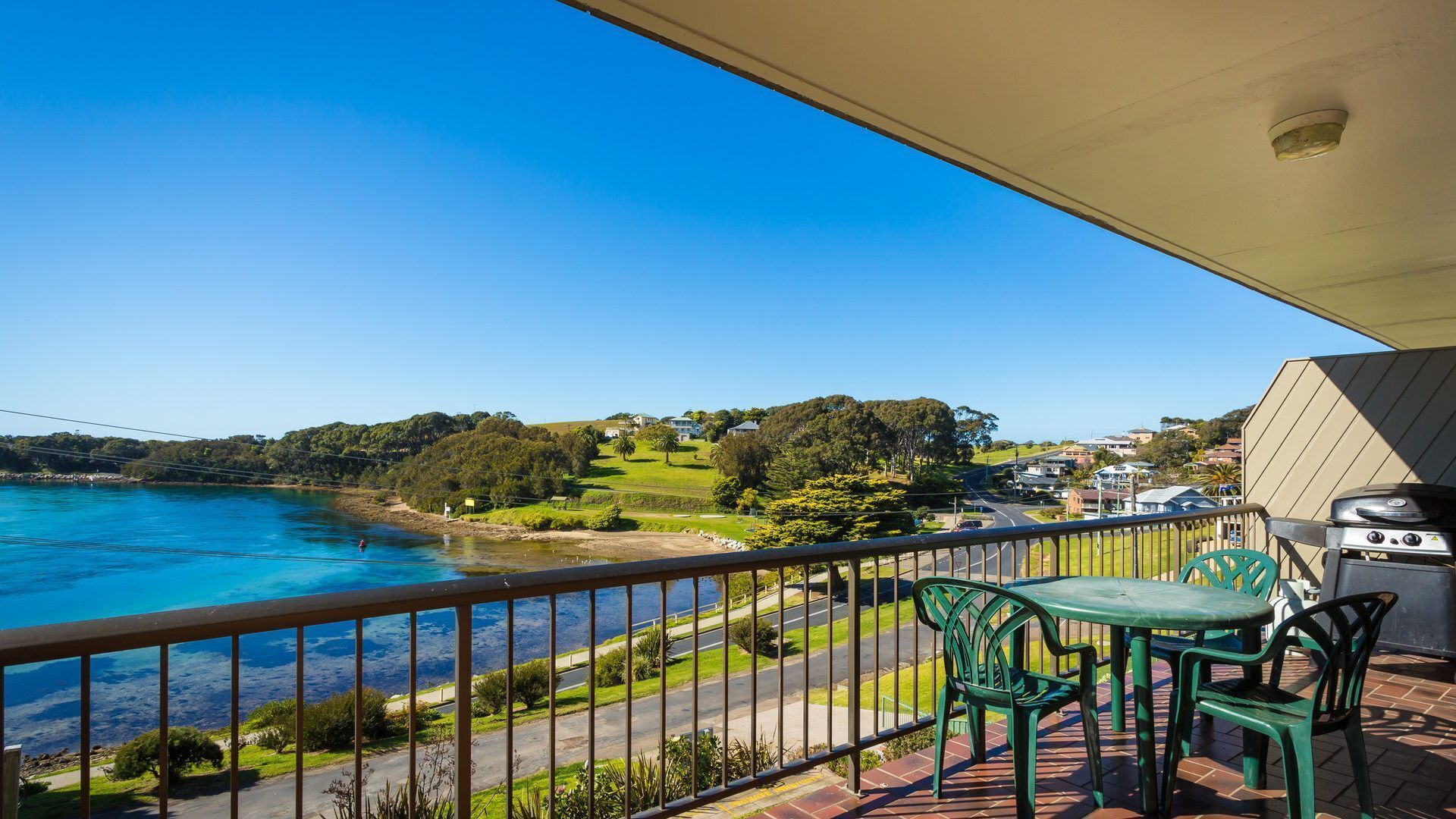 Un balcon avec vue sur une rivière, des chaises vertes, une table et un barbecue.