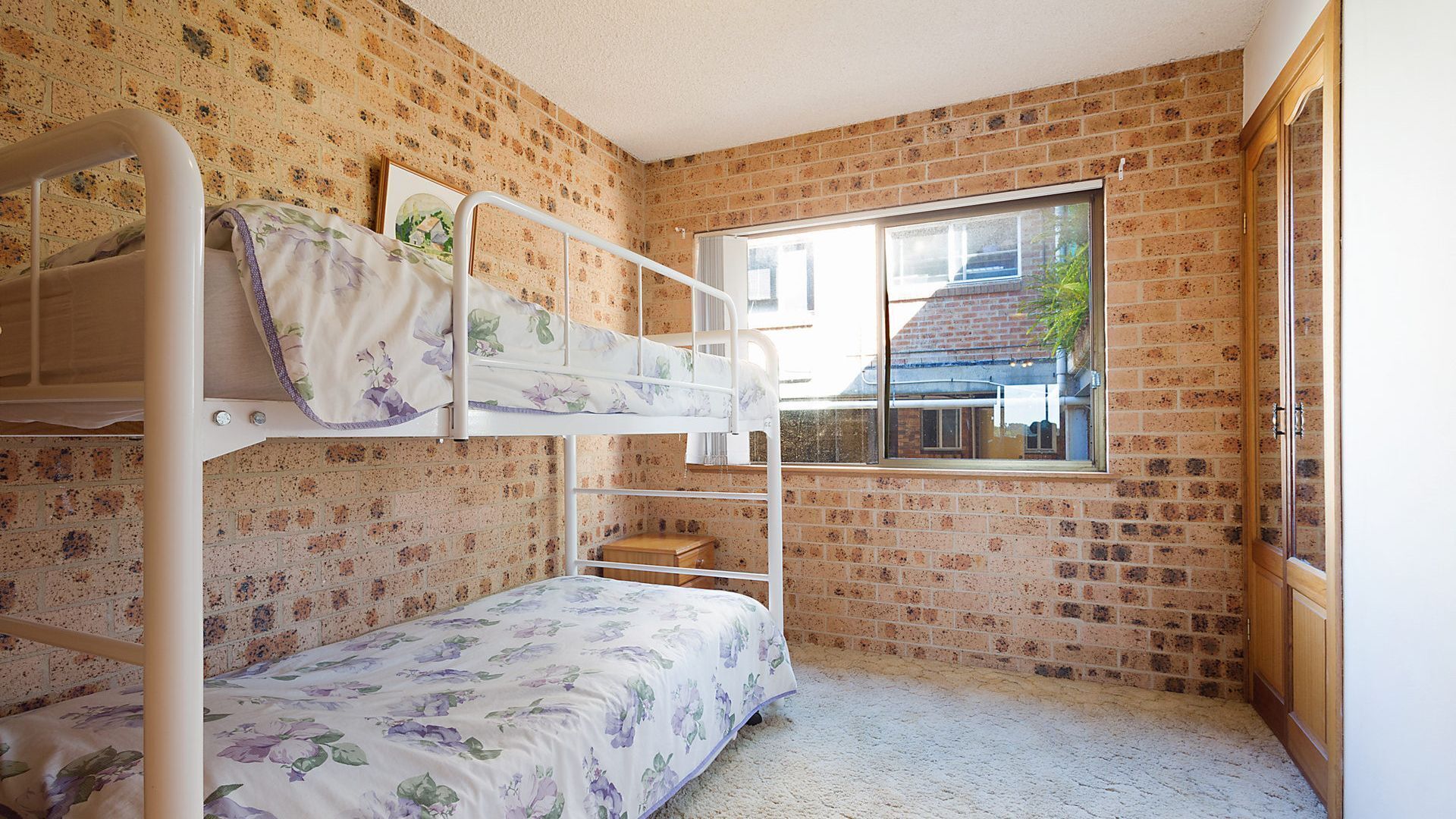 Une chambre avec un lit superposé, un mur en briques, une fenêtre et une armoire en bois.