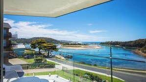A balcony with a clear view of a river, a beach, and a hilly landscape.