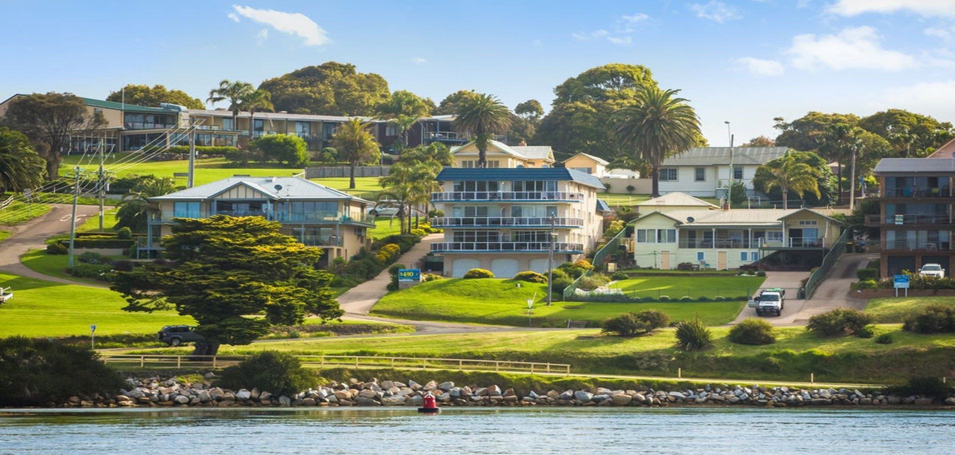 A coastal residential area with houses, a clear view of the sea, and a rocky shoreline.