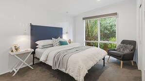 A bedroom with a bed, bedside table, chair, and a large window with a view of greenery.