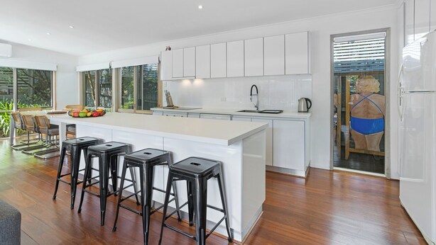 A modern kitchen with white cabinetry, a central island with stools, and a view of the outdoors through large windows.