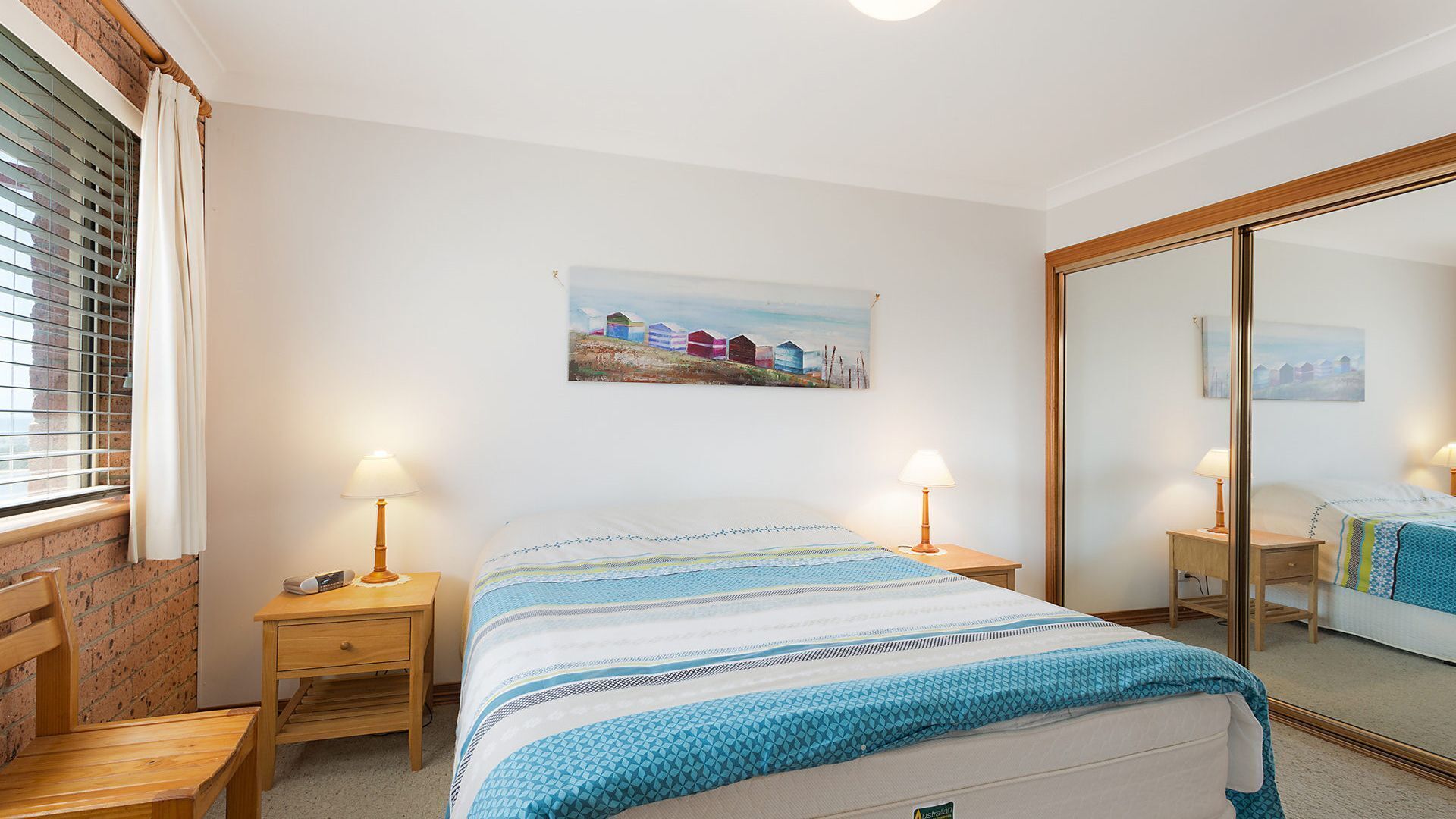 A bedroom with a bed, bedside tables, a nightstand, a mirror, and a painting on the wall.