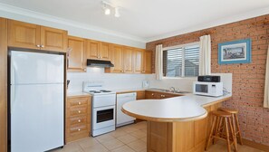 Kitchen features a refrigerator, stove, oven, microwave, and sink, with a brick wall and window.