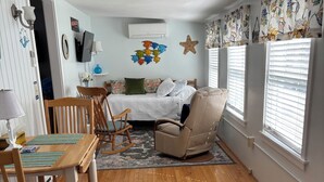 Ein Zimmer mit Holzboden, einem Bett mit gemusterten Betttextilien, einem Esstisch mit Stühlen und einer Seestern-Dekoration an der Wand.