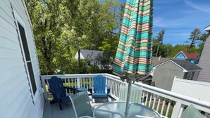 Eine Terrasse mit einem Tisch und Stühlen mit Glasplatte, einem gestreiften Sonnenschirm und einem weißen Geländer.