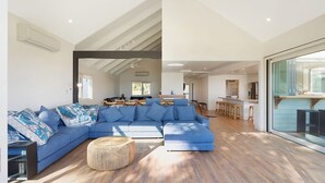 Ein modernes Wohnzimmer mit einer Eckcouch, einem runden Weidenhocker und einem Essbereich mit Barhocker.
