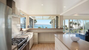 Eine moderne Küche mit Meerblick, ausgestattet mit Edelstahlgeräten, einem großen Fenster und einem minimalistischen Design.