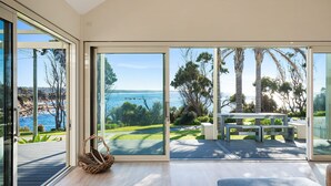 Ein modernes Interieur mit großen Glasüren, die auf eine Terrasse mit Blick auf das Meer und viel Grün führen.