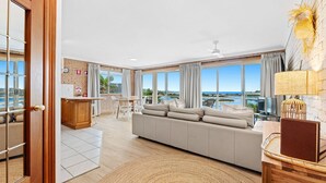A spacious living area with a large sofa, a dining table, and a kitchen area. - Grand Pacific 1 Unit 1 - Ground Floor (NAROOMA)